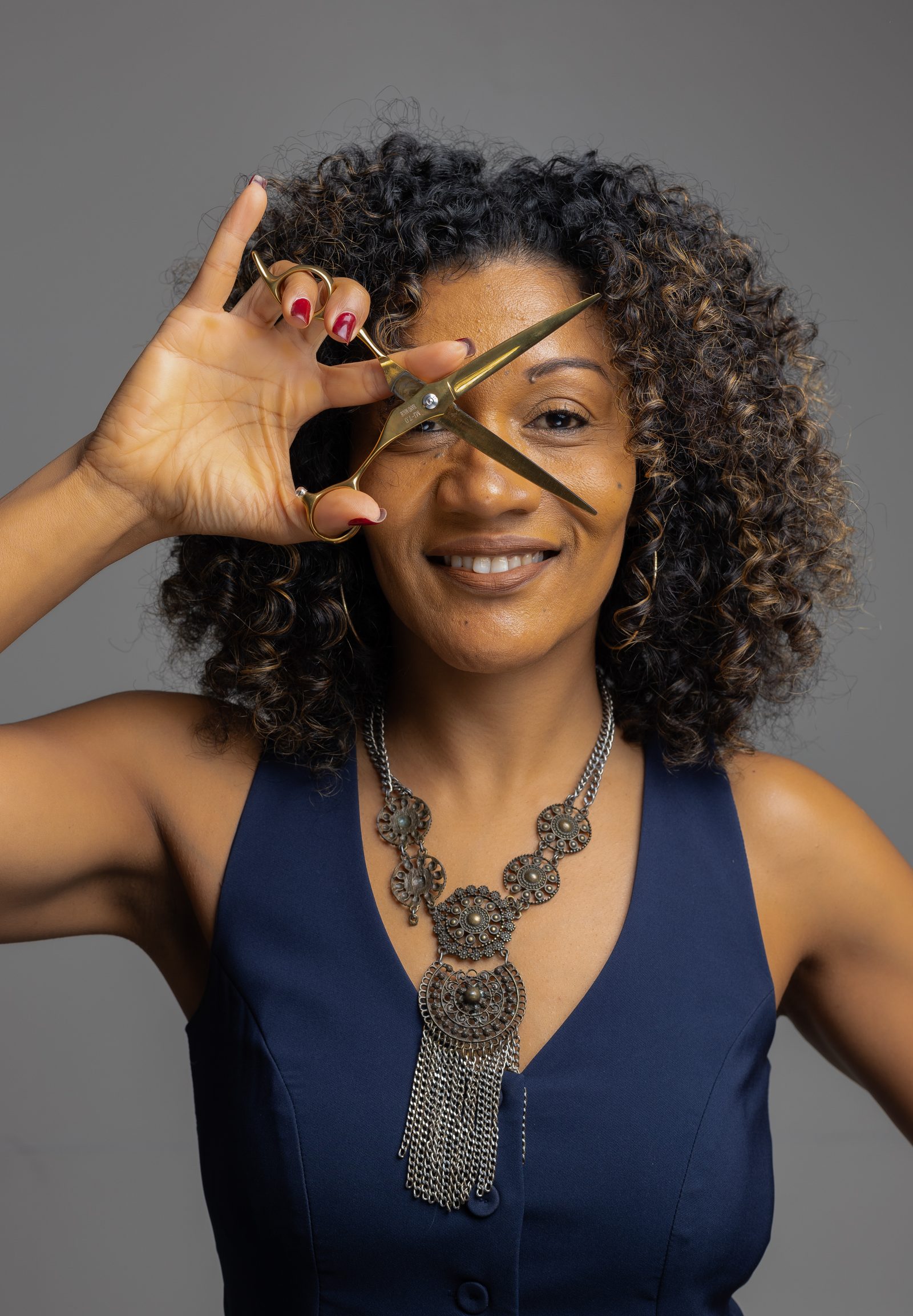 Retrato de Eliane Carvalho sorrindo com a tesoura em frente ao olho.